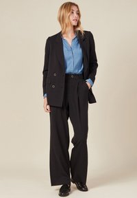 Blazer noir à double boutonnage avec des détails en or, associé à une chemise bleu clair et un pantalon noir à jambes larges. Textures lisses et design structuré.