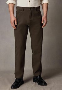 Bruine broek van gladde stof, met een klassiek ontwerp, rechte pijpen en zijzakken, gecombineerd met zwarte schoenen.