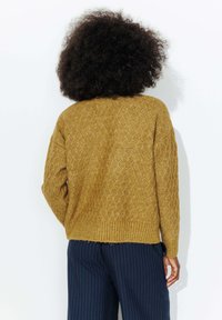 Pull en maille jaune moutarde avec un motif en losanges texturé, ourlet côtelé et épaules tombantes, associé à un pantalon bleu marine à rayures.