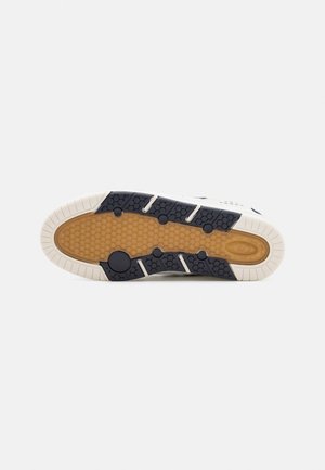 Skoens sål med beige tekstureret midte og sorte gummigrebsektioner langs kanterne på en hvid baggrund.