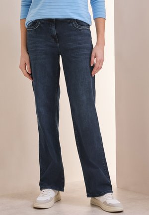 Jeans en denim bleu foncé avec une coupe droite, dotés de coutures contrastantes, de poches avant et d'une taille mi-haute. Portés avec des baskets blanches.