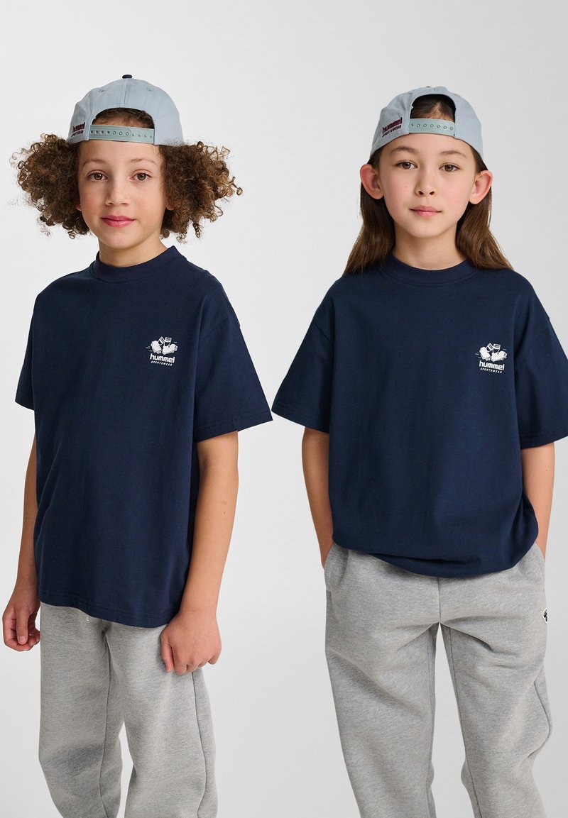 Mörkblå t-shirts i bomull med korta ärmar, med en liten vit logotyp på vänster bröst, kombinerat med gråa sweatpants.