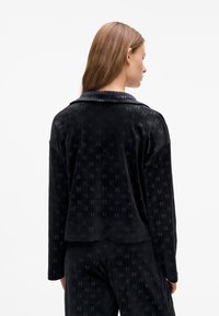 Giacca in velluto nero con un sottile motivo a logo, vestibilità comoda e colletto, dotata di maniche lunghe e tessuto testurizzato.