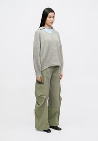 Hall hallitatud oversize-kampsun kraega, kombineeritud lahtiste roheliste cargo-pükstega, millel on suured taskud ja tekstuuriga kangas. Mustad kingad.