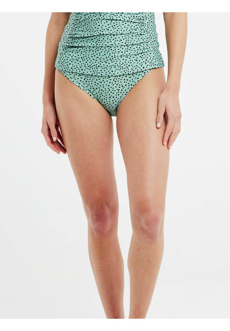 Mėtų žalios spalvos maudymosi kostiumėlis su sukaupta medžiaga ir juodomis taškeliais; turi prigludusią viršutinę dalį ir aukštu taliju, kad suteiktų dailią siluetą.