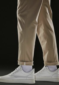 Adidași din piele albă cu talpă plată, cu ochiuri metalice și accente gri, asortați cu pantaloni bej răsuciți și șosete albe.
