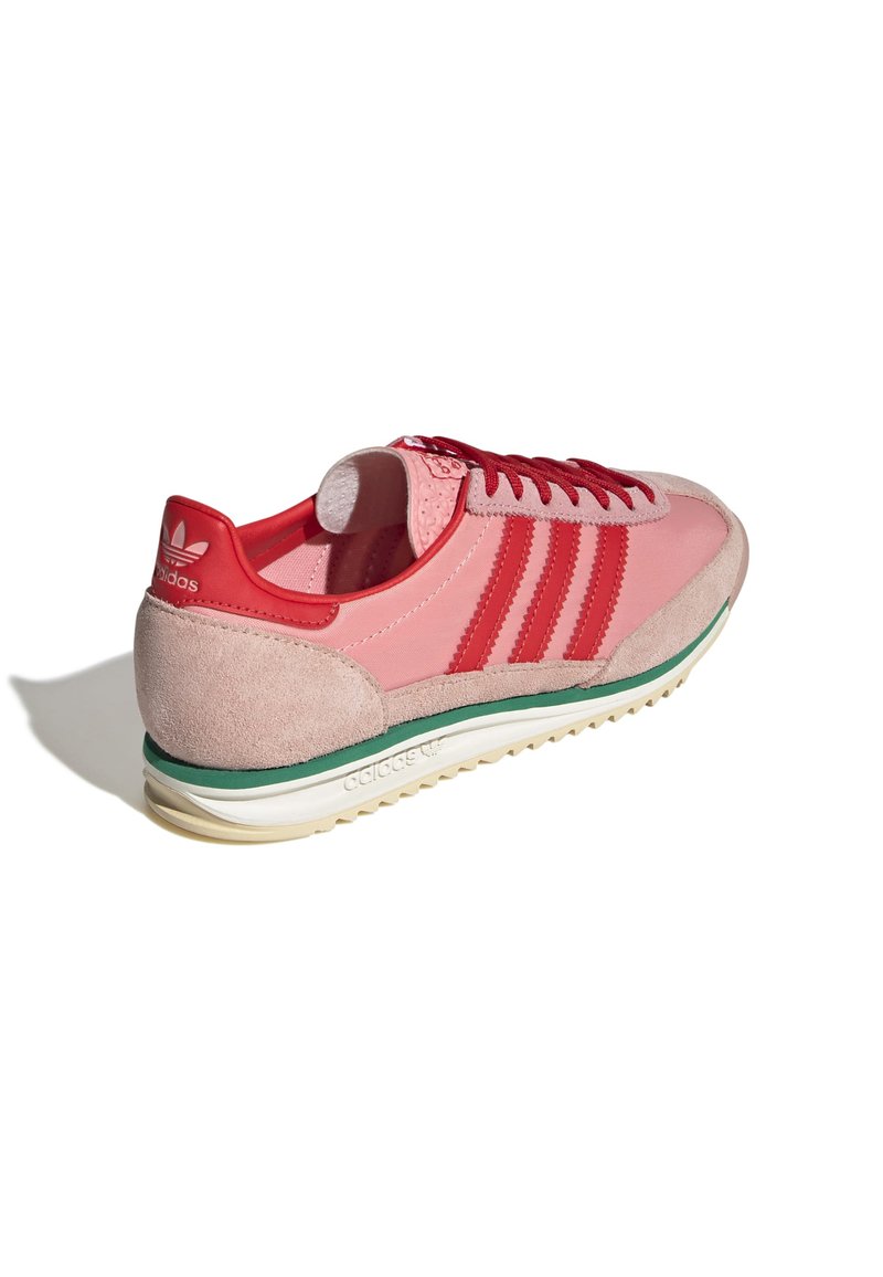 Baskets de sport roses en matériaux suédés et synthétiques, avec des accents rouges et trois bandes, semelle verte et talon texturé.