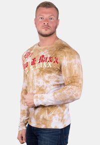 Langemouwen shirt met een tie-dye patroon in tinten van bruin en wit, met rode graphics op de borst en arm. Gemaakt van een katoenmix.
