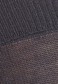 Tecido negro de malha texturada com secção superior canelada e secção inferior lisa e transparente. Costura visível ao longo da junta.