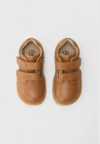 Καφέ δερμάτινα παπούτσια με δύο ιμάντες βέλκρο, στρογγυλεμένη μύτη και υφασμένο καουτσούκ στη σόλα. Εσωτερική επένδυση με λογότυπο στην πάτο.