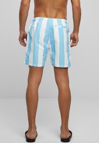 Blaue und weiße gestreifte Badeshorts mit elastischem Bund und einer Gesäßtasche mit Reißverschluss. Das Material wirkt glatt und leicht.