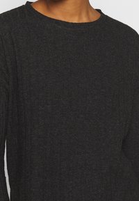 Czarna bluzka z długim rękawem wykonana z miękkiej, teksturowanej tkaniny z prążkowanym wzorem i okrągłym dekoltem, o luźnym kroju.