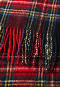 Sciarpa di lana con un motivo a quadri rosso, nero e verde, con accenti gialli e bianchi. Il dettaglio frangiato aggiunge texture e contrasto.