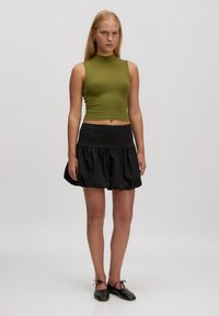 Olijfgroen geribbeld crop top gecombineerd met een zwarte uitlopende mini-jurk. De outfit heeft een getailleerd ontwerp met een gladde textuur en een brede tailleband.