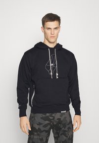 Felpa nera con un design grafico sul davanti, dotata di cappuccio con cordoncino e tasca con zip. Pantaloni con motivo mimetico completano l'outfit.