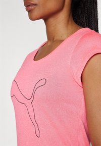 Närbild av en person som bär en rosa skjorta med en svart kontur av en hoppande puma-logotyp på bröstet.