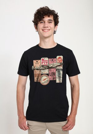 Sort t-shirt med et grafisk design, der indeholder vintage rejsetags og en illustration af et fly i forskellige farver, herunder pink, hvid og brun.