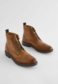 Botas de cuero marrón con detalles de brogue, punta redondeada, cordones en la parte delantera y suela de goma con un tirador en la parte trasera.