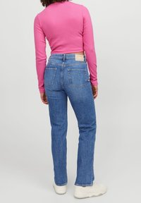 En figursydd rosa långärmad topp med rund halsringning som är kombinerad med blå högmidjade denimjeans med bakfickor och en sydd etikett.