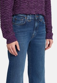 Maglione a maglia viola con motivo a onde, abbinato a jeans in denim blu con taglio classico e design a cinque tasche standard.