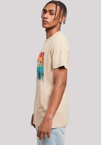 Beige katoenen t-shirt met een kleurrijke berglandschap grafiek in blauw, oranje en bruin, met korte mouwen en een klassieke pasvorm.