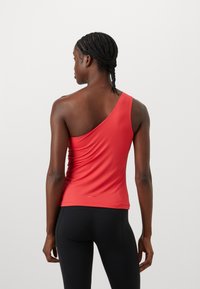 Red one-shoulder top made of smooth fabric, featuring a fitted design with gathered detailing on the side and a small logo at the hem.