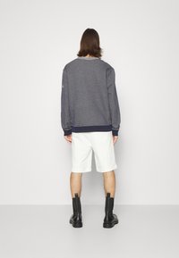 Sudadera gris con puños y dobladillo acanalados, pantalones cortos blancos y botas negras hasta el tobillo. Diseño simple, tela texturizada y colores contrastantes.