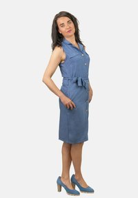 Vestido de mezclilla con cuello, botones en la parte delantera y cinta en la cintura, que presenta dos bolsillos en el pecho y un corte recto hasta la rodilla en un tejido azul claro.