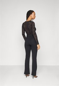 Black lace long-sleeve top paired with fitted black pants. The top features floral patterns and a round neckline. Boots complete the look.