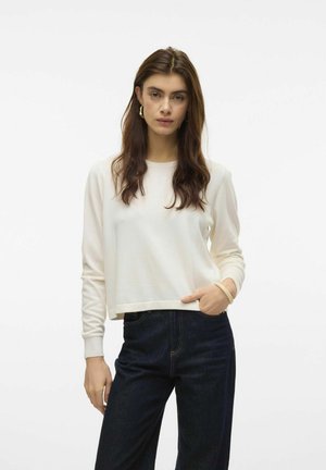 Sweatshirt accorciato a manica lunga di colore crema, con scollatura tonda e polsini a coste, abbinato a jeans di denim scuro.