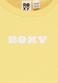Sudadera amarilla de tejido suave con un gran texto blanco "ROXY" en una fuente negrita y redondeada. Cuello acanalado para un ajuste ceñido.
