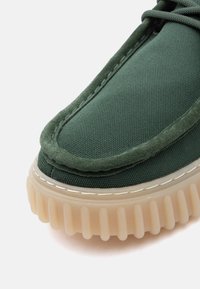 Πράσινο ύφασμα παπούτσι με σουέντ περιμετρικά και παχύ ραβδωτό ημιδιάφανο μπεζ πέλμα, στενή λήψη στην περιοχή τω ν δαχτύλων.