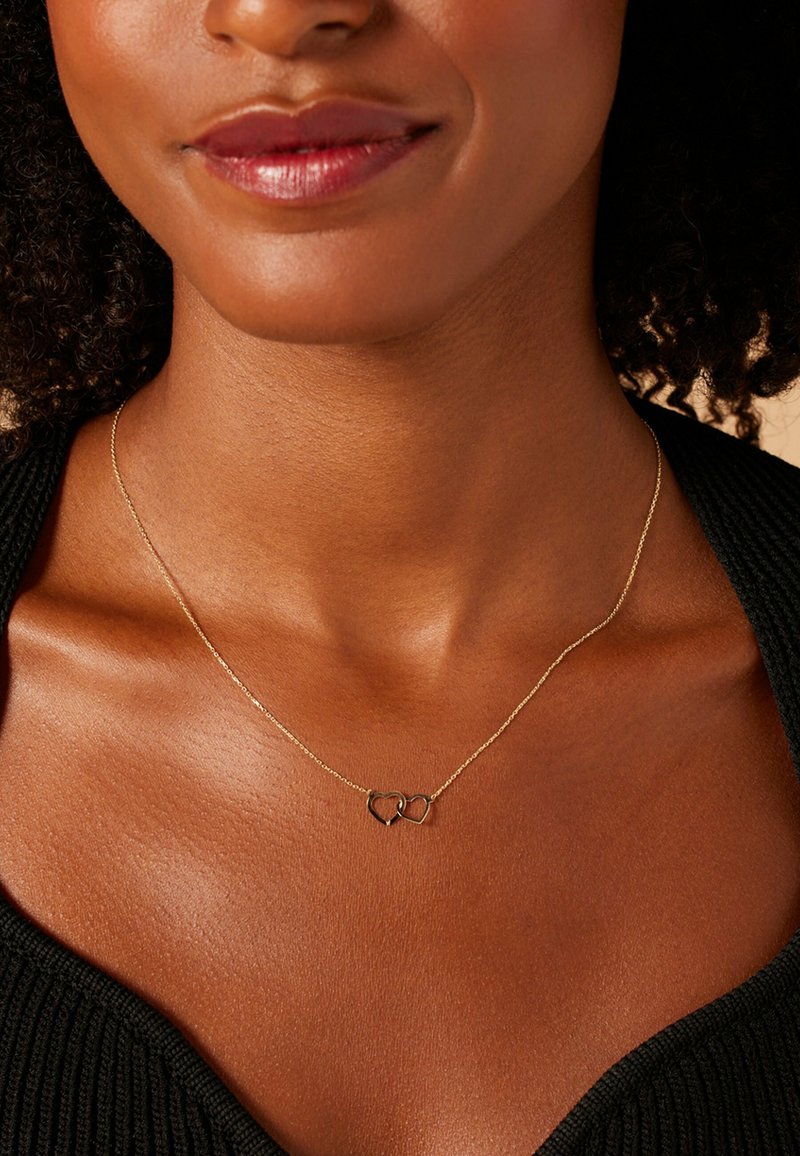 Gouden ketting met twee ineengestrengelde hartbedels, gladde metalstructuur, fijne schakels en een minimalistisch ontwerp.