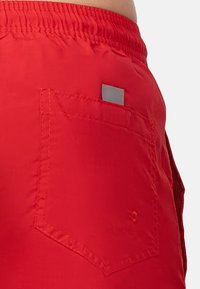 Pantaloni da bagno rossi con una tasca a patta e un accento rettangolare. Il tessuto è morbido con una leggera lucentezza; cintura elastica per il comfort.