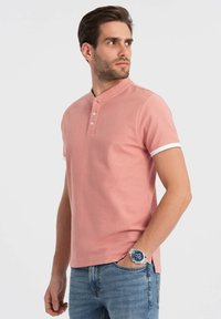 Lyserød kortærmet polo t-shirt med henley-udskæring, tre knaplukninger og hvide detaljer på ærmerne. Båret med blå jeans.