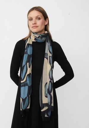 Letvægts tørklæde i beige med abstrakte blå og sorte mønstre. Blød tekstur med frynser i kanterne, elegant draperet omkring halsen.