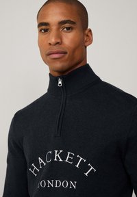 Marinefarbener Reißverschluss-Pullover mit hohem Kragen, aus strukturiertem Strick und mit weißem "HACKETT LONDON"-Logo auf der Brust.