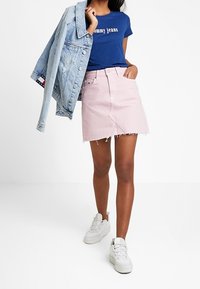 Jeansjacka, blå T-shirt med "Tommy Jeans"-logotyp, rosa minikjol med fransad fåll, vita sneakers. Avslappnad outfit med lager på lager-färger.