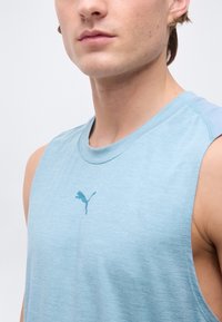 Κοντινό πλάνο ενός ατόμου που φοράει αμάνικη μπλούζα Puma ανοιχτού μπλε χρώματος, με ορατό λαιμό, ώμους και λογότυπο στο στήθος.