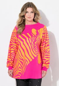 T-shirt a maniche lunghe, oversize, di un vivace rosa con un grande motivo a strisce gialle tipo zebra. Materiale in cotone morbido con polsini a coste.