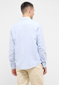 Camicia a righe blu chiaro con colletto classico, polsini abbottonati e orlo curvato. Realizzata in tessuto intrecciato con una texture liscia.