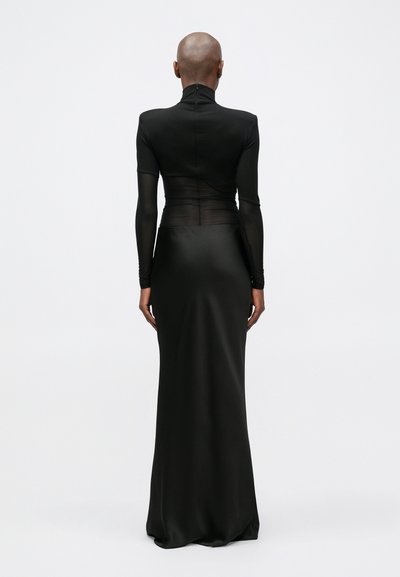 Rochie de seară neagră cu guler înalt și mâneci lungi, având panouri superioare translucide și o siluetă conformată, curgând către o fustă amplă.