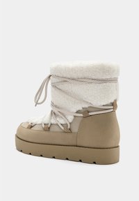 Botas de tobillo beige con puño de piel sintética blanca, aseguradas por cordones plateados, con una suela gruesa y parte superior texturizada para calidez y comodidad.