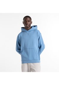 Sudadera con capucha azul claro, confeccionada en tela suave, cuenta con un bolsillo frontal y un pequeño logo en el pecho izquierdo. Textura lisa, ajuste holgado.