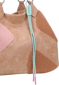 Tan leren tas met textuurpatches in roze en bruin, met een mintgroene strap en roze uiteinden, wat een uniek ontwerp accentueert.
