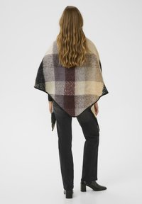Plaid poncho in soft wool blend featuring large check patterns in cream, brown, and black. Edges are finished with a subtle trim.