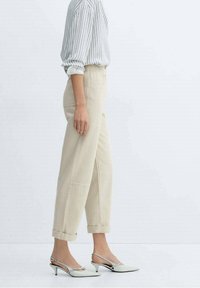 Pantaloni beige a vita alta con risvolti e tasche frontali, abbinati a scarpe bianche con punta appuntita e tacco basso. Top a righe, dal taglio largo.