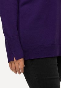 Maglione viola a maglia con orlo e polsini texturizzati, caratterizzato da spacchi laterali. Indossato sopra jeans neri, mette in evidenza una vestibilità rilassata e un materiale morbido.