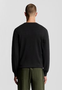 Zwarte trui met een ronde hals, lange mouwen en een getailleerde pasvorm. Draagt over groene cargobroek, minimale textuur is zichtbaar.