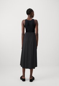 Black tank top paired with a long, flowy black skirt featuring an elastic waist. Smooth texture with a relaxed fit. Black platform sandals.
